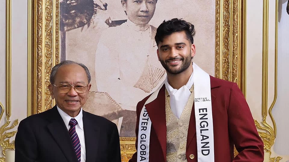 Baltej Tattla wearing a sash that reads Mr England on it. He is smiling and shaking hands with someone.